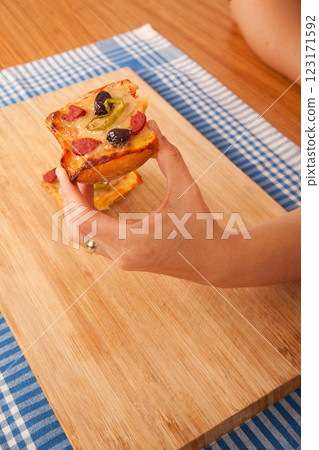 Caucasian white person holding pizza pieces on bamboo cutting board on blue napkin Caucasian white person holding pizza pieces on bamboo cutting board on blue napkin 123171592