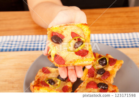 Caucasian white person holding pizza pieces on bamboo cutting board and gray plate on blue napkin Caucasian white person holding pizza pieces on bamboo cutting board and gray plate on blue napkin 123171598