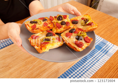 Caucasian person with fair skin holding tasty pizza pieces in gray plate on blue napkin and bamboo cutting board, Caucasian person with fair skin holding tasty pizza pieces in gray plate on blue napkin and bamboo cutting board, 123171604
