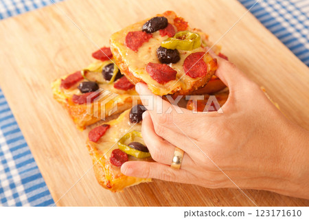 Caucasian white person holding pizza pieces on bamboo cutting board on blue napkin Caucasian white person holding pizza pieces on bamboo cutting board on blue napkin 123171610
