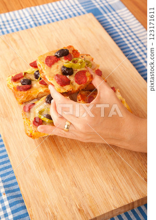Caucasian white person holding pizza pieces on bamboo cutting board on blue napkin Caucasian white person holding pizza pieces on bamboo cutting board on blue napkin 123171611