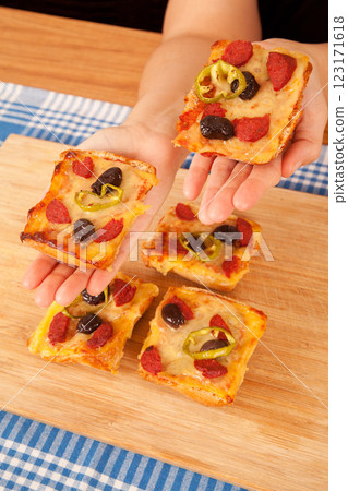 Caucasian white person holding pizza pieces on bamboo cutting board on blue napkin 123171618