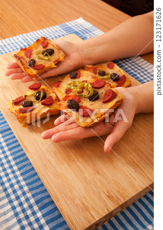 Caucasian white person holding pizza pieces on bamboo cutting board on blue napkin Caucasian white person holding pizza pieces on bamboo cutting board on blue napkin 123171626