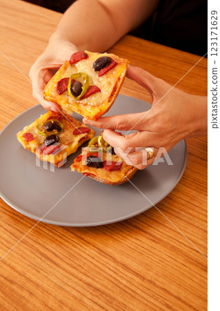 Caucasian white person holding delicious pizza slices in grey plate on wooden table 123171629