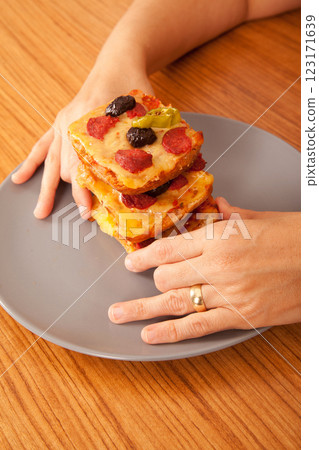 Caucasian white person holding delicious pizza slices in grey plate on wooden table Caucasian white person holding delicious pizza slices in grey plate on wooden table 123171639