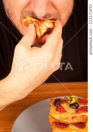 Bearded Caucasian white mature man in black t-shirt eating delicious pizza slices in a gray plate on a table 123171652