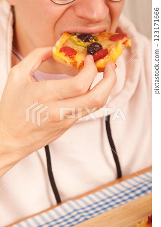 Bearded Caucasian white young male wearing pink t-shirt eating delicious pizza slices on bamboo cutting board on table 123171666