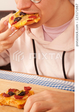 Bearded Caucasian white young male wearing pink t-shirt eating delicious pizza slices on bamboo cutting board on table 123171667