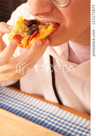 Bearded Caucasian white young male wearing pink t-shirt eating delicious pizza slices on bamboo cutting board on table 123171675