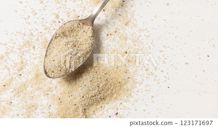Raw uncooked fonio seeds in a metal spoon on white table, top view. African ancient pseudocereal 123171697