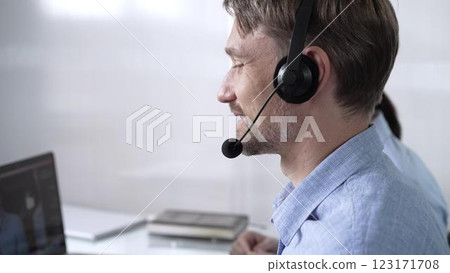 Focused male call center operator in blue casual shirt is assisting clients online, providing customer support and answering inquiries. Call center 123171708