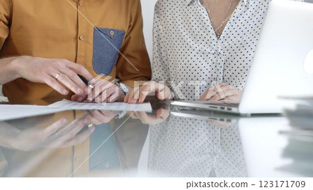Two accountants are discussing a tax audit, using a laptop and reviewing documents at a glass table. Taxes, audit in business 123171709