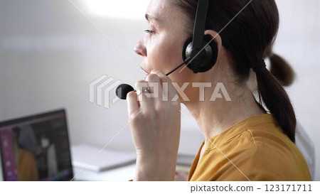 Focused female call center operator in yellow casual blouse is assisting clients online, providing customer support and answering inquiries. Call center concept 123171711