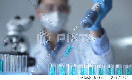 Close up of a female scientist researcher hand using a micropipette to fill up test tubes with a blue liquid in laboratory. Medicine and science 123171773