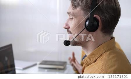 Focused male call center operator in yellow casual shirt is assisting clients online, providing customer support and answering inquiries. Call center operators 123171801