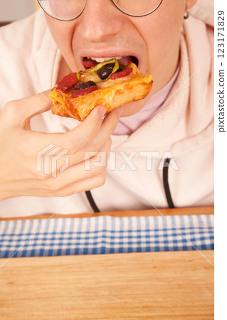Bearded Caucasian white young male wearing pink t-shirt eating delicious pizza slices on bamboo cutting board on table Bearded Caucasian white young male wearing pink t-shirt eating delicious pizza slices on bamboo cutting board on table 123171829