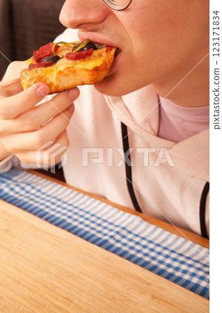 Bearded Caucasian white young male wearing pink t-shirt eating delicious pizza slices on bamboo cutting board on table Bearded Caucasian white young male wearing pink t-shirt eating delicious pizza slices on bamboo cutting board on table 123171834