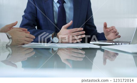 Business partners or lawyers dressed in blue are reviewing and discussing contract papers during a meeting, using a laptop and documents on a glass table. Businesspeople 123172014