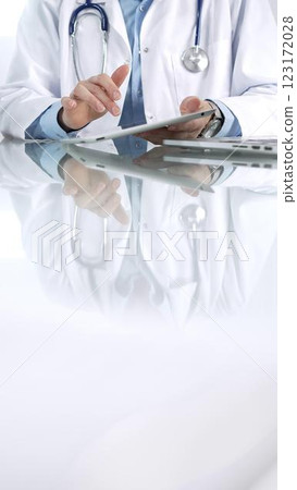 Unrecognizable female doctor in blue blouse, stethoscope and white coat is using digital tablet in modern healthcare setting, interacting with patient data, vertical view. Medicine and science 123172028
