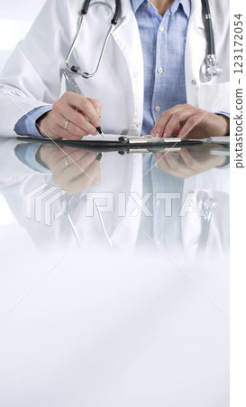 Unrecognizable doctor man in a blue shirt under a medical coat, is using a clipboard and taking notes on glass desk in a medical office, close-up vertical view. Medicine and health care Unrecognizable doctor man in a blue shirt under a medical coat, is using a clipboard and taking notes on glass desk in a medical office, close-up vertical view. Medicine and health care 123172054