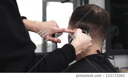 Skilled barber trimming client's hair using electric razor, creating contemporary hairstyle in modern barbershop setting with precise, professional technique 123172062
