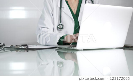 Female doctor using technology in healthcare, close up of hands typing on laptop with stethoscope, glasses, and clipboard on desk Female doctor using technology in healthcare, close up of hands typing on laptop with stethoscope, glasses, and clipboard on desk 123172065
