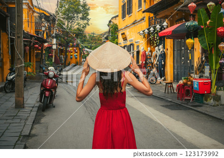back of a young beautiful woman tourist in a traditional Vietnamese hat and red dress on street in the old town in Hoi An city in Vietnam in Asia 123173992