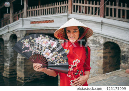 happy female traveler tourist in a Vietnamese hat at ancient Japanese covered bridge in Hoi An in Vietnam in Asia 123173999