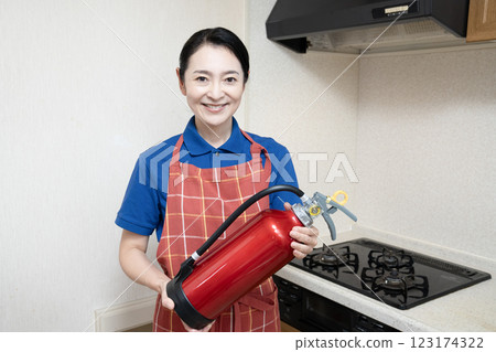 Smiling woman holding a fire extinguisher in the kitchen Smiling woman holding a fire extinguisher in the kitchen 123174322