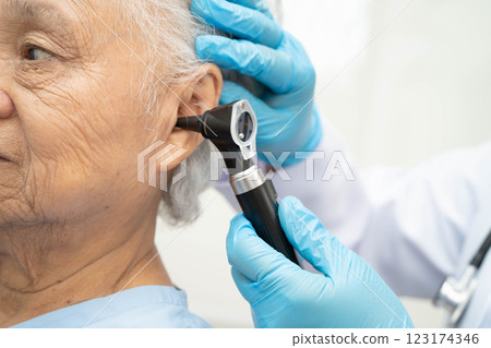 Otolaryngologist or ENT physician doctor examining senior patient ear with otoscope, hearing loss problem. 123174346
