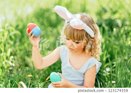 Easter egg hunt. Girl child Wearing Bunny Ears Running To Pick Up Egg In Garden. Easter tradition. Baby with basket full of colorful eggs. Easter egg hunt. Girl child Wearing Bunny Ears Running To Pick Up Egg In Garden. Easter tradition. Baby with basket full of colorful eggs. 123174359