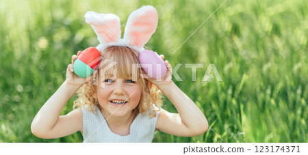Easter egg hunt. Girl child Wearing Bunny Ears Running To Pick Up Egg In Garden. Easter tradition. Baby with basket full of colorful eggs. Easter egg hunt. Girl child Wearing Bunny Ears Running To Pick Up Egg In Garden. Easter tradition. Baby with basket full of colorful eggs. 123174371