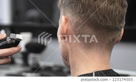Skilled barber trimming client's hair with electric razor, demonstrating professional grooming technique in modern barbershop interior 123174503