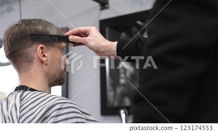 Barber carefully combing hair, client wearing protective cape, preparing for precision styling inside sleek contemporary barbershop setting 123174553