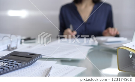 Black calculator, pen and documents are lying on accountant's desk. Businesswoman wearing blue dress is working with documents on the background. Business and audit concept 123174568
