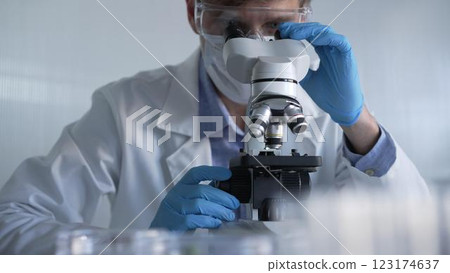 Male scientist researcher wearing blue gloves, protective glasses and medical mask, is using microscope in modern laboratory, portrait view. Low key lighting photo. Science and Medicine Male scientist researcher wearing blue gloves, protective glasses and medical mask, is using microscope in modern laboratory, portrait view. Low key lighting photo. Science and Medicine 123174637