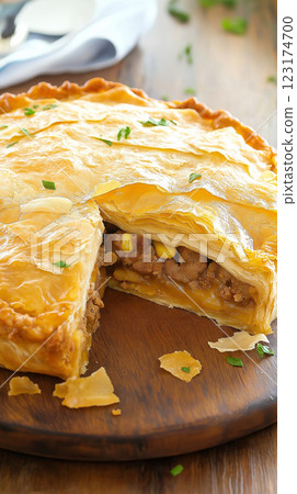 freshly baked layered meat and vegetable pie with crispy caramelized crust on rustic wooden board, golden flaky top with delicate layers, crunchy crumbs scattered, warm lighting, concept of bakery, 123174700