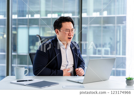 Upset Businessman Experiencing Discomfort While Working at a Modern Office Desk 123174966