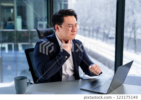 Asian Businessman with Sore Throat in Modern Office with Laptop Asian Businessman with Sore Throat in Modern Office with Laptop 123175149