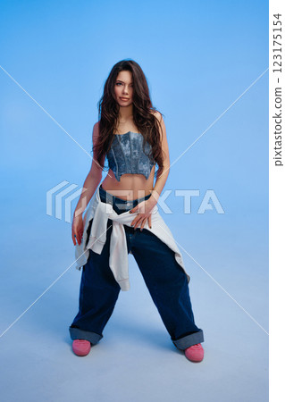 Young woman poses confidently in casual streetwear against blue backdrop Young woman poses confidently in casual streetwear against blue backdrop 123175154