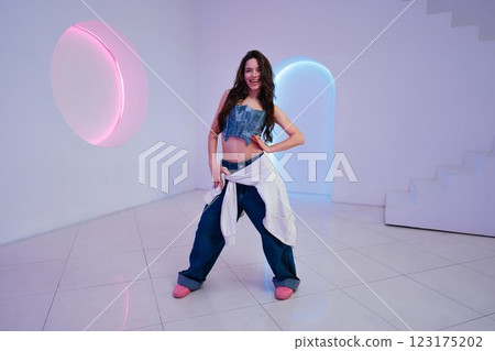 Young woman posing confidently in modern studio with colorful lighting 123175202