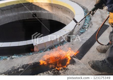 An industrial worker uses fire to soften a rubber underlay for floor insulation, showcasing precision and skill in a critical step of the construction process 123175349
