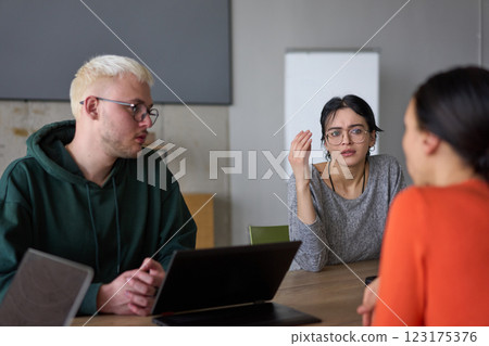 A young, diverse business team sitting together in a modern office, exchanging ideas and business plans, fostering collaboration and innovation for future success. 123175376