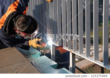 Industrial welder skillfully crafts a metal fence for a new business complex, using modern equipment that casts bright sparks and highlights the precision and dedication of the craft. Industrial welder skillfully crafts a metal fence for a new business complex, using modern equipment that casts bright sparks and highlights the precision and dedication of the craft. 123175404