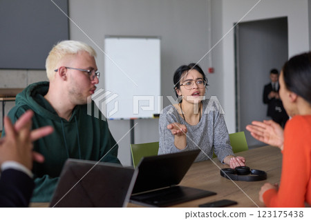 A young, diverse business team sitting together in a modern office, exchanging ideas and business plans, fostering collaboration and innovation for future success. 123175438
