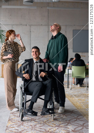 Group cheerful business colleagues, including a businessman in a wheelchair, posing together in a modern office, showcasing teamwork and inclusivity 123175526