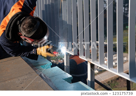 Industrial welder skillfully crafts a metal fence for a new business complex, using modern equipment that casts bright sparks and highlights the precision and dedication of the craft. Industrial welder skillfully crafts a metal fence for a new business complex, using modern equipment that casts bright sparks and highlights the precision and dedication of the craft. 123175739