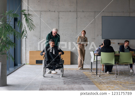 A diverse team of business colleagues, including a director in a wheelchair, engages in a collaborative discussion as they move together through a modern office space A diverse team of business colleagues, including a director in a wheelchair, engages in a collaborative discussion as they move together through a modern office space 123175789