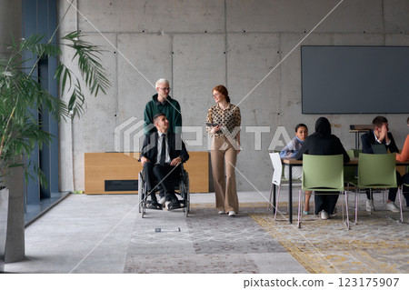 A diverse team of business colleagues, including a director in a wheelchair, engages in a collaborative discussion as they move together through a modern office space 123175907