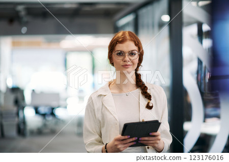 A business woman with orange hair self confident, fully engaged in working on a tablet, exuding creativity, ambition and a lively sense of individuality A business woman with orange hair self confident, fully engaged in working on a tablet, exuding creativity, ambition and a lively sense of individuality 123176016
